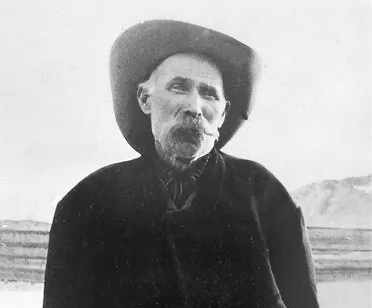Montillus 'Old Man' Beatty in a wide-brimmed hat and heavy coat, standing in the open desert